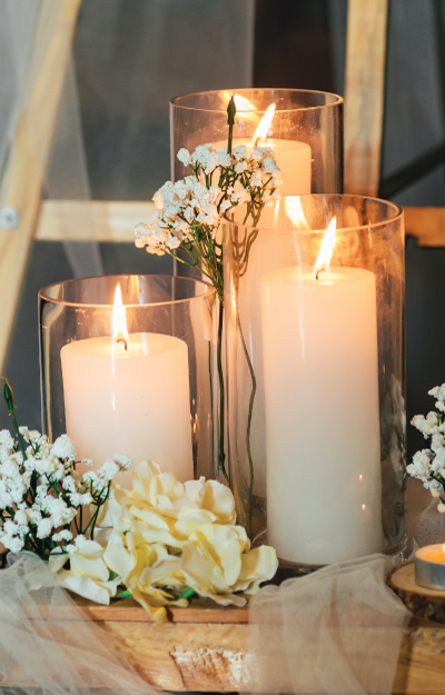 three white pillar candles with flames on a table with flowers
